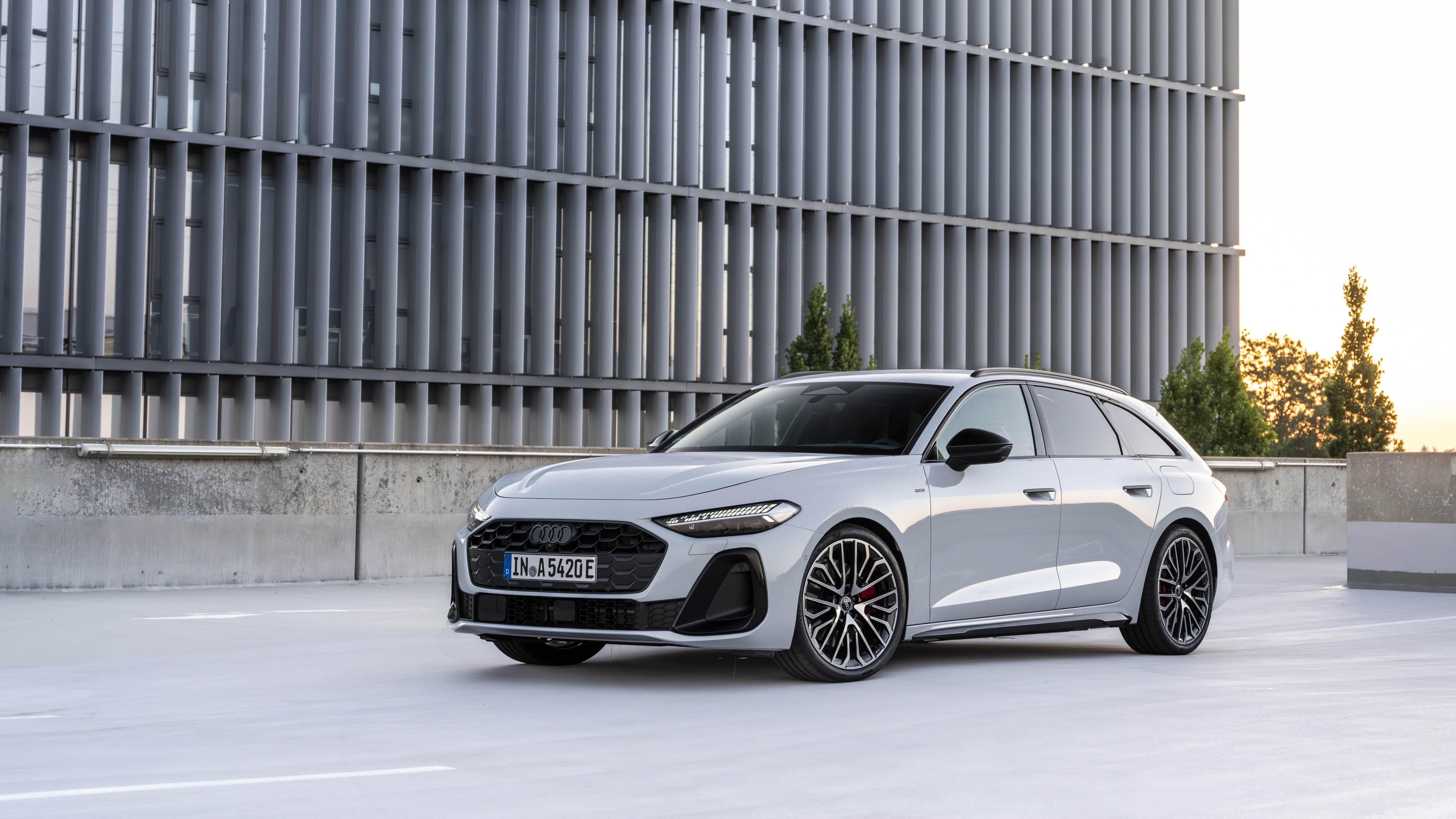 Ein weißer Audi A5 Avant e-hybrid quattro parkt vor einem futuristischen Gebäude.