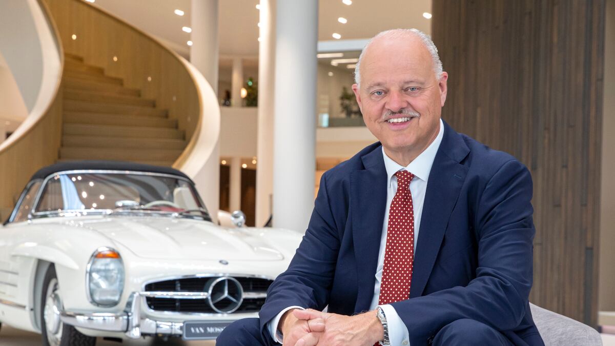 Eric Berkhof sitzt auf einem modernen Hocker in einem Autohaus-Showroom. Im Hintergrund steht ein Mercedes-Oldtimer.